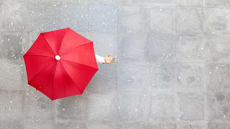 Overhead shot of a red umbrella in the rain, highlighting the benefits of umbrella insurance.