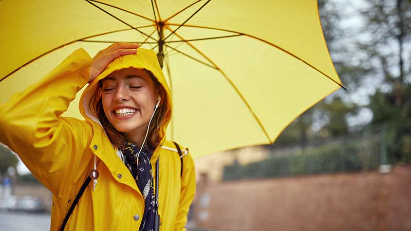 Smiling woman under a yellow umbrella, representing the peace of mind provided by umbrella insurance.