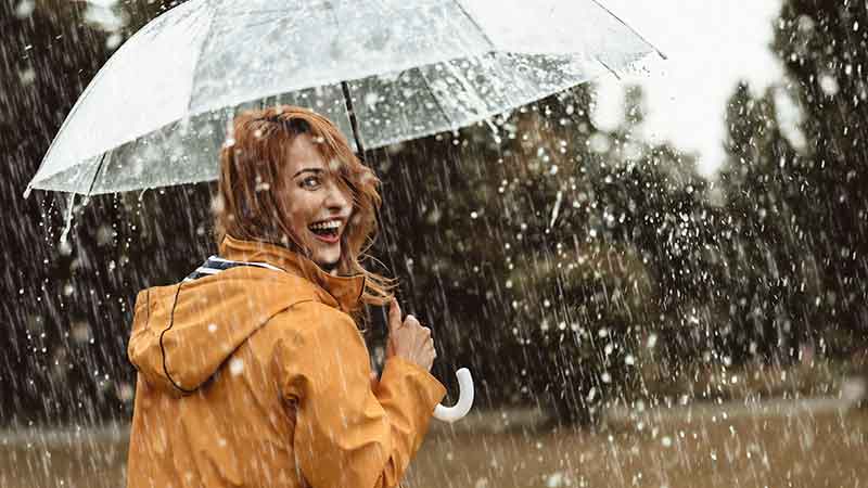 Laughing woman with a clear umbrella, depicting the peace of mind provided by umbrella insurance.