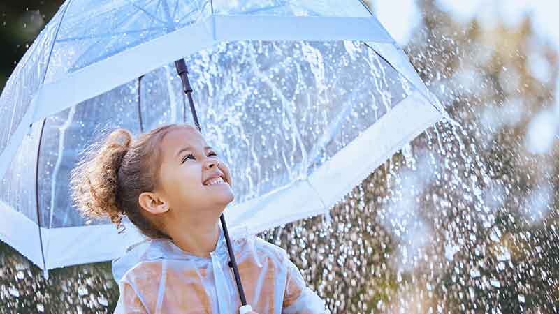 a little girl stands under an umbrella in the rain, protected from getting wet. Much like you are in financial catastrophe if you have an umbrella insurance policy