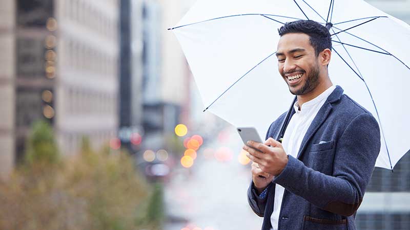 Businessman using a smartphone under a white umbrella, illustrating the convenience of umbrella insurance.